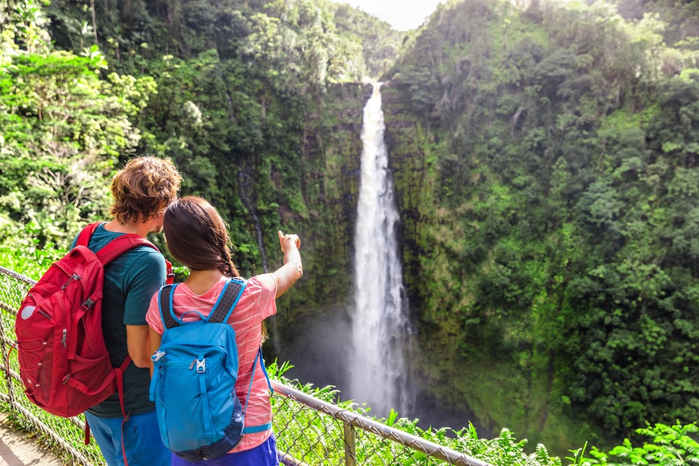 Couple tourists on Hawaii by waterfall. Tourist girl pointing at Akaka Falls waterfall on Hawaii, Big Island, USA.