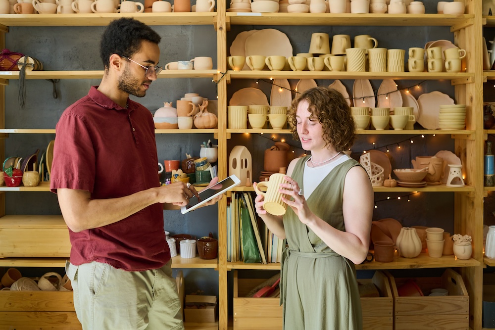 Young female holding handmade clay mug during discussion with colleague