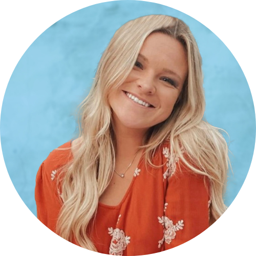 Smiling woman with long blonde hair wearing an orange floral top, against a light blue background.