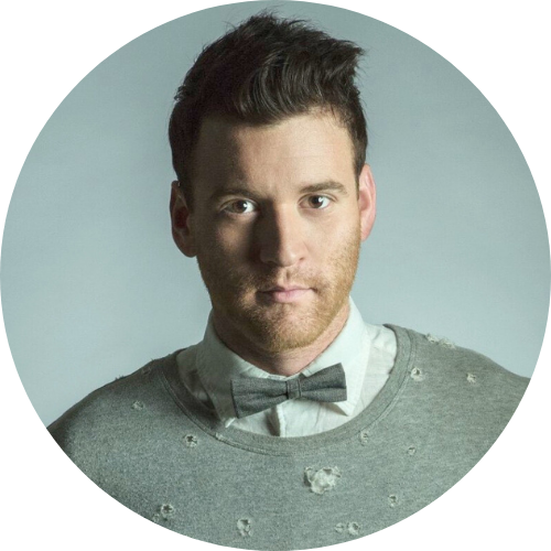 Head-and-shoulders portrait of a man with dark hair wearing a gray sweater and bow tie in a neutral setting to the camera.