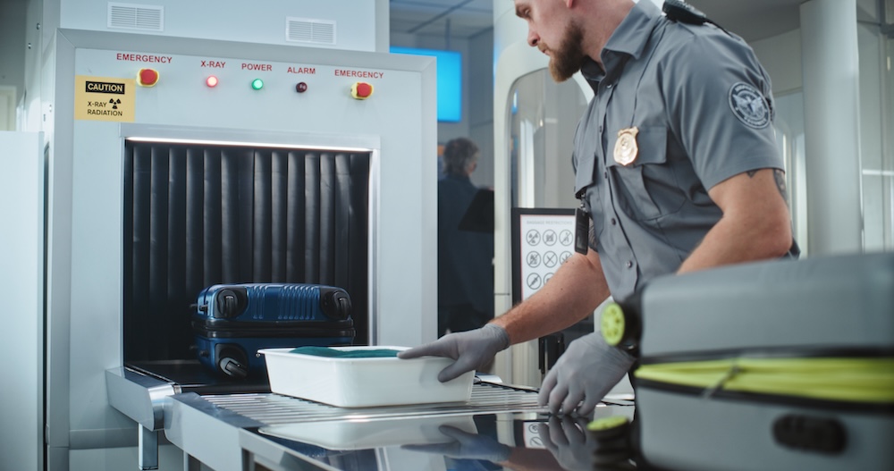 Security Officer Putting Suitcases and Personal Items in Trays on Conveyor Belt with X-ray Scanning.