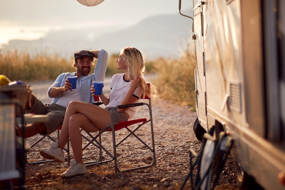 Couple at sunset cheering with drinks. Sitting in front of camper rv.